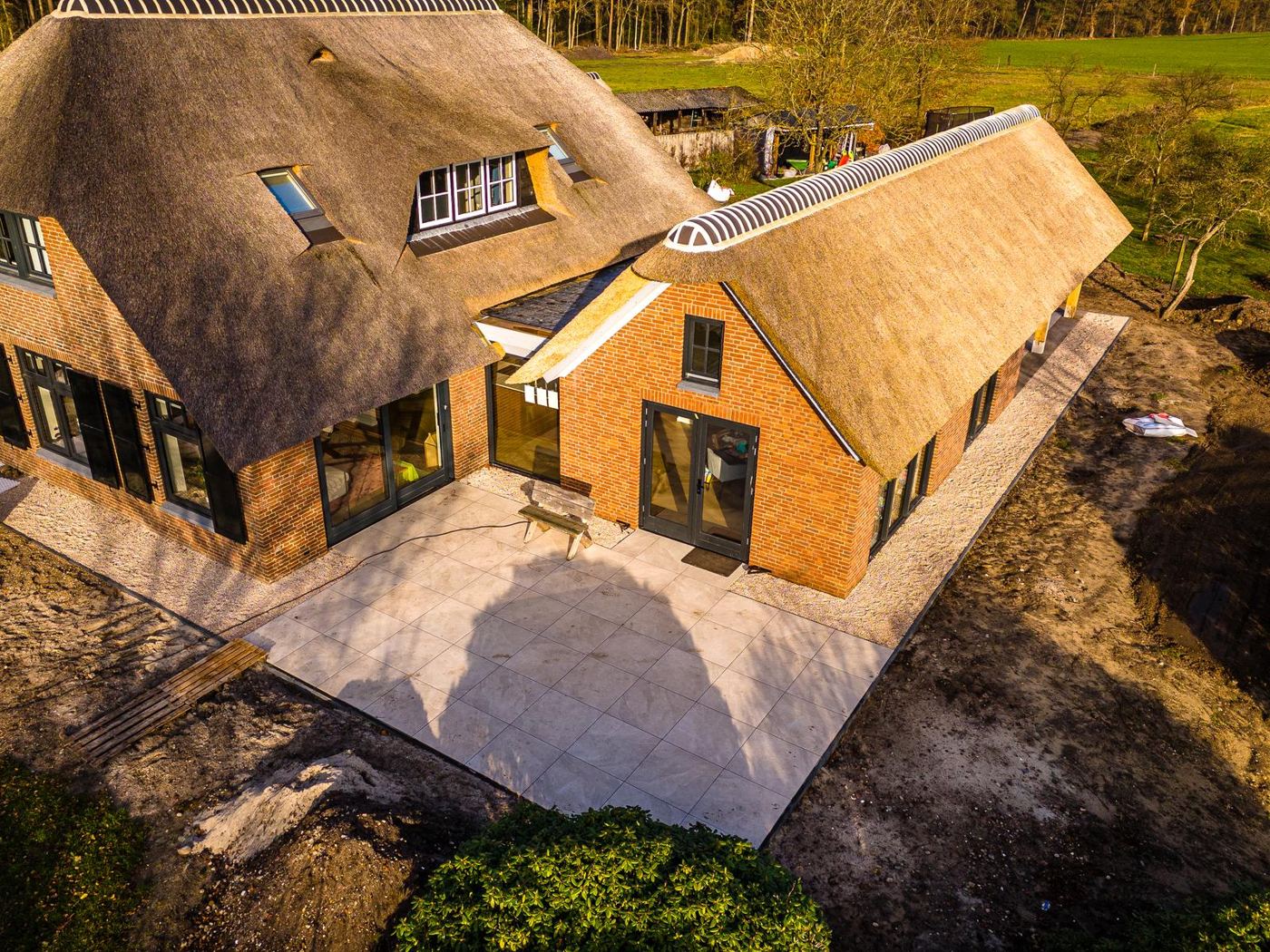 Rieten woning met nieuwe bakstenen uitbouw en groot terras, gezien van boven