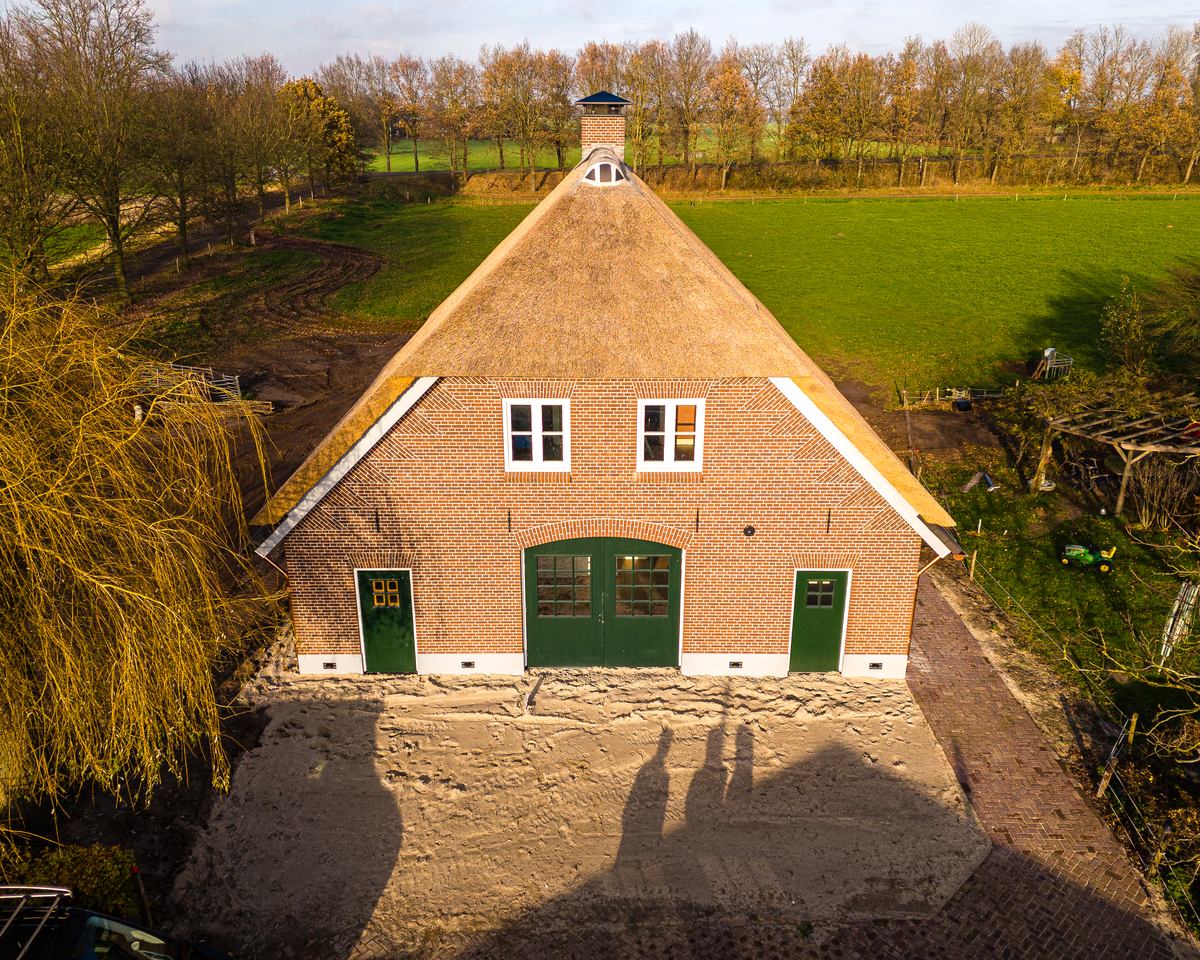 Woning met rieten kap, bakstenen gevel en groene deuren, gezien van voren