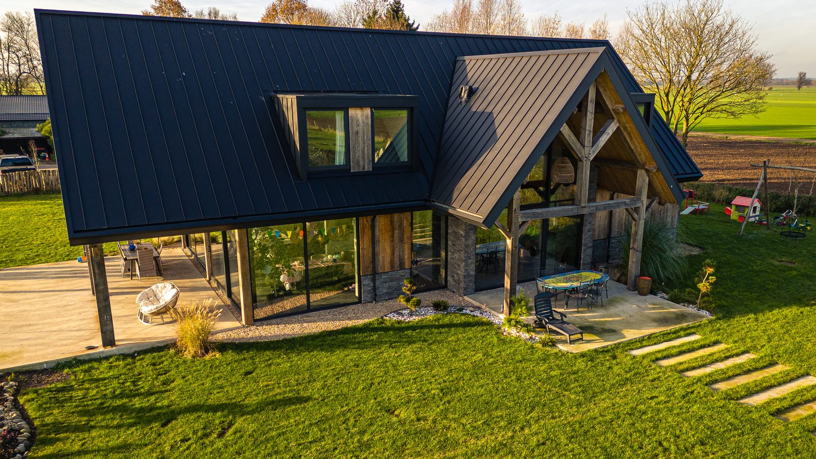 Nieuw gebouwde woning met donker dak en houten spanten, veel glas en een terras aan de tuin