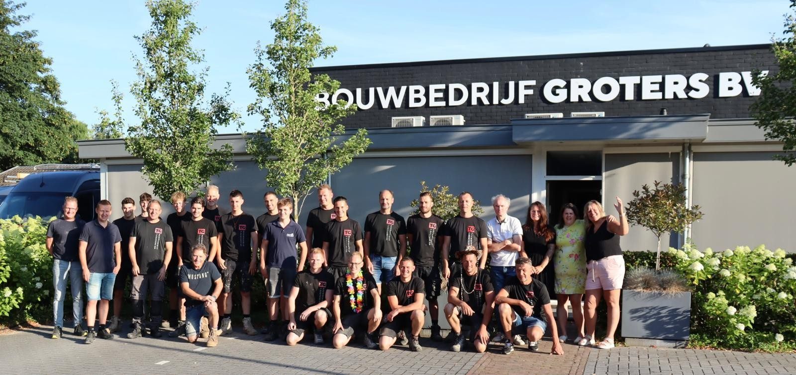 Het team van Bouwbedrijf Groters staat samen voor het bedrijfspand met de naam Bouwbedrijf Groters op de gevel