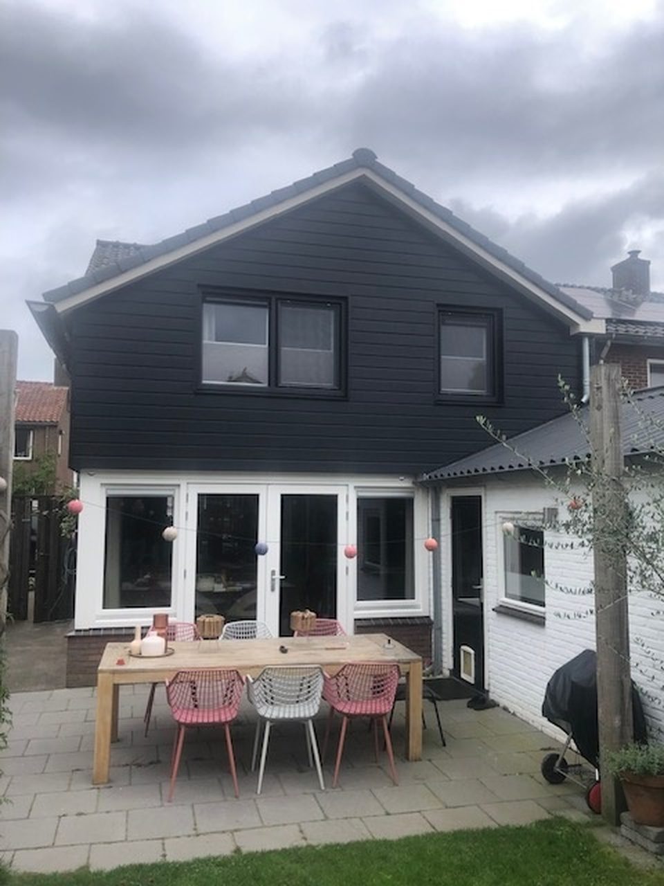 Na: de opgeleverde achtergevel met donkere gevelbekleding, openslaande deuren en een gedekte tafel in de tuin