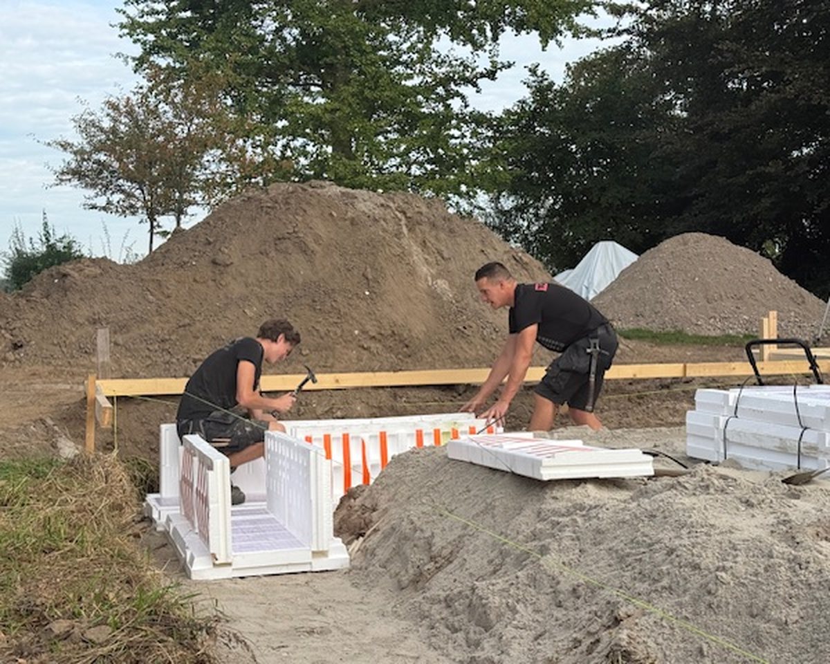 Twee collega's van Groters in zwarte werkkleding leggen samen witte bekistingselementen voor een fundering