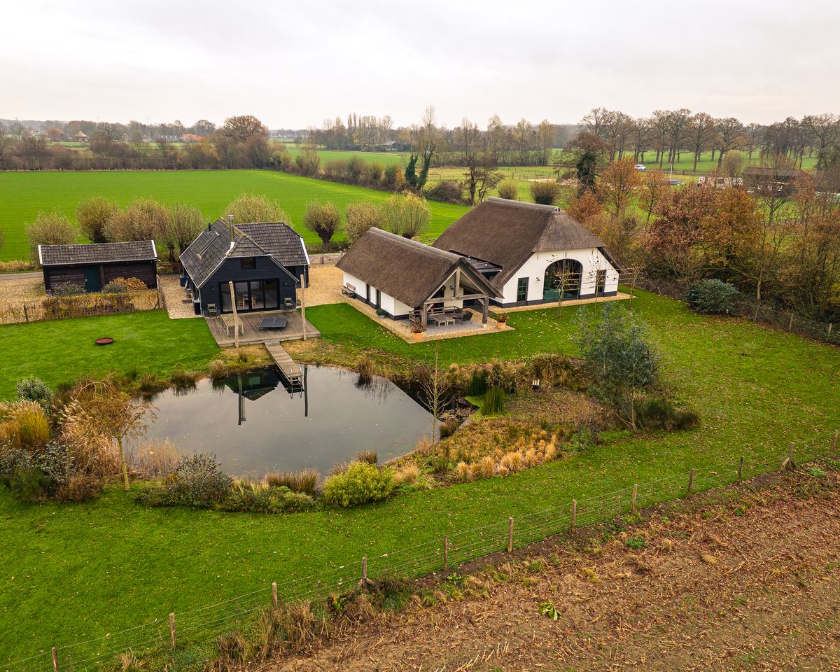 Witte boerderij met rieten kap en zwarte bijgebouwen aan een vijver